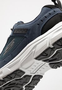 Niebiesko-czarne buty sportowe z fakturowanej tkaniny, wzmocnionym czubkiem, masywną białą podeszwą środkową oraz wzorzystą gumową podeszwą.