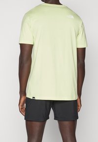 Svetle zelené tričko s krátkým rukávem a kulatým výstřihem, na zadní straně s logem, v kombinaci s černými šortkami. Měkký bavlněný materiál.