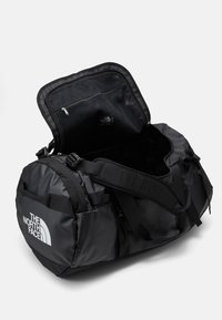 Svart duffel bag med en slitesterk, vannavvisende ytterflate, som har en stor åpning og en intern mesh-lomme. Logoen er vist fremtredende.