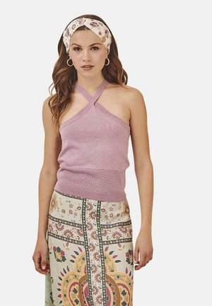 Top halter de punto rosa claro con tirantes cruzados, combinado con una falda larga estampada con diseños florales en colores apagados.