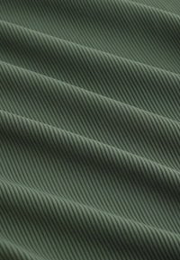 Zelená látka s jemnou diagonální žebrovanou strukturou a měkkými záhyby vytvářejícími paralelní stínované linie.