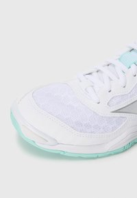 White athletic shoe with mesh upper, turquoise accents on the sole, and textured pattern. Features traditional lacing and a rounded toe.