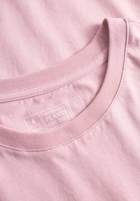 Rosa Baumwoll-T-Shirt mit geripptem Rundhalsausschnitt und einem Etikett mit Text auf einem glatten Stoff. Das Design ist minimalistisch, ohne Muster oder Akzente.