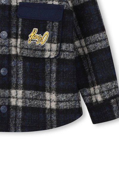 Veste en laine plaid bleu marine et gris avec des boutons sur le devant, une poche à rabat et un logo "Kenzo Paris" brodé en jaune sur la poche poitrine.