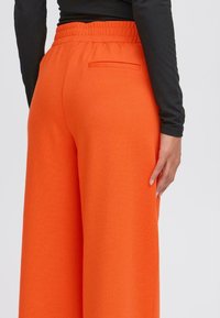 Oranje wijde broek van een gestructureerde stof met een elastische tailleband. Heeft een achterzak en subtiele stiksel details.