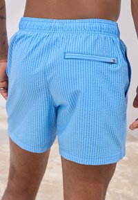 Herrbadbyxor i ljusblått med ett strukturerat vertikalt randmönster, elastisk midja och en enda bakficka med dragkedjedetalj.