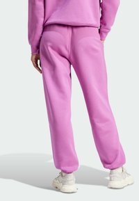 Rosa mjukisbyxor med avslappnad passform, texturert tyg, elastiskt midjeband och muddar. Kombineras med vita sneakers. Bakifrån visar en slät design.