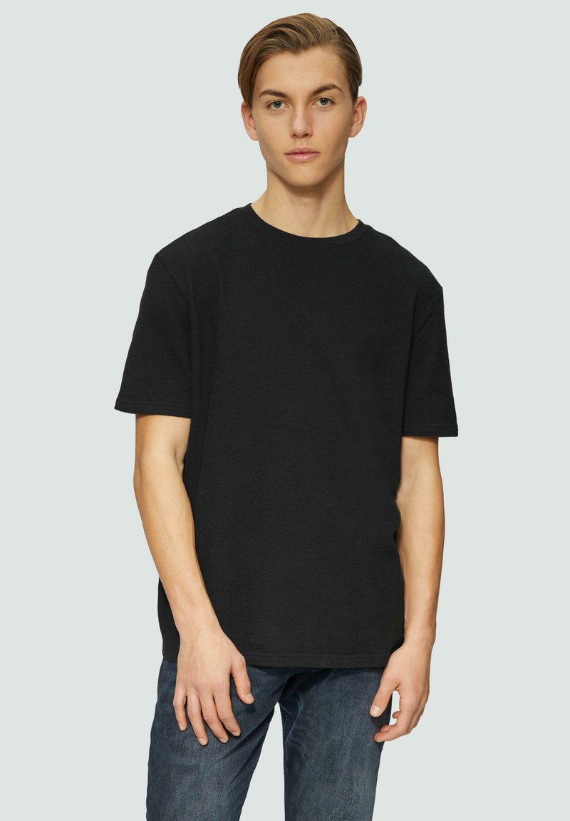 T-shirt en coton noir avec un col rond et des manches courtes. Design simple, coupe légèrement ample, associé à un jean bleu. Texture lisse.