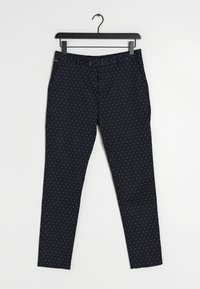 Pantaloni blu navy con pois bianchi, realizzati in un tessuto liscio, dotati di zip, passanti per cintura e tasche laterali. Appesi a una gruccia nera.
