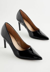 Musta patenttina nahkakengät, joissa on terävä kärki ja 4-tuuman stilettikorko. Sisäpuolella on sileä vaaleanbeige vuori.
