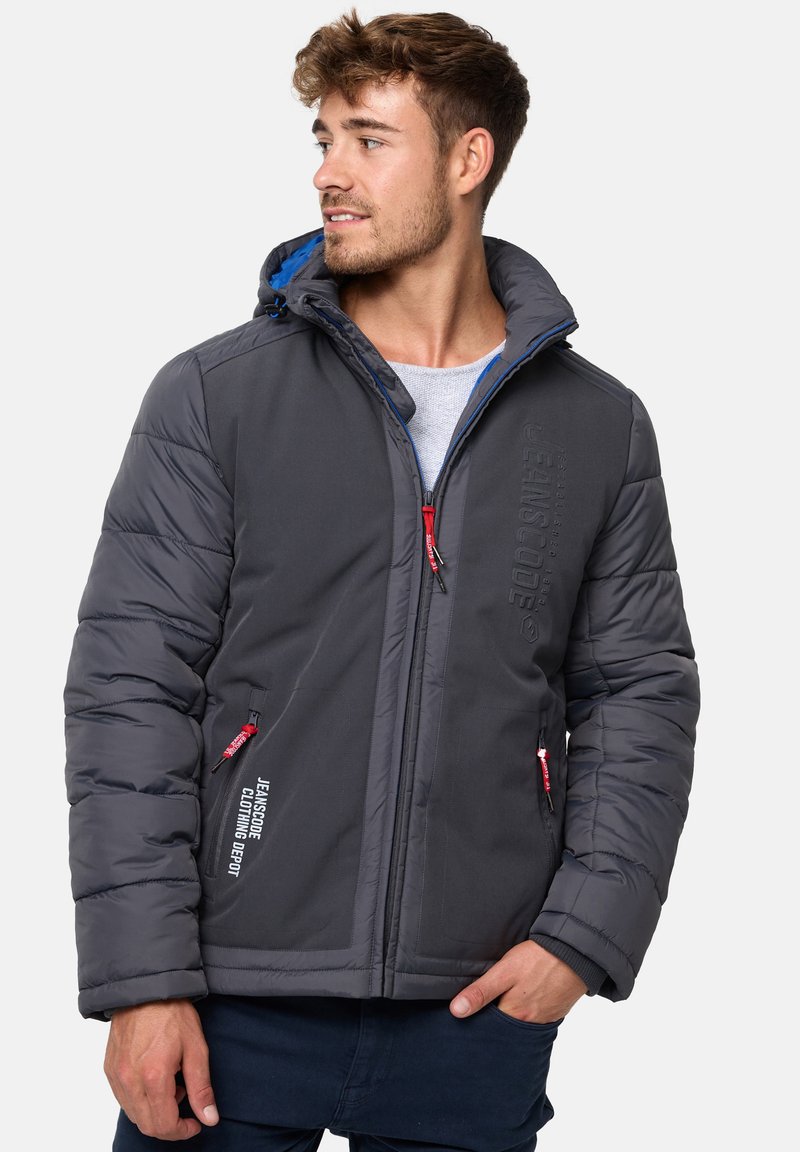 Veste isolée grise avec capuche, featuring zips rouges, doublure bleue, manches matelassées et détails de marque en relief à l'avant.