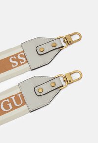 Pasek płócienny w biało-brązowy paskowany wzór, z elementami ze skóry i złotymi klamrami. Detale przeszycia zapewniają trwałość.