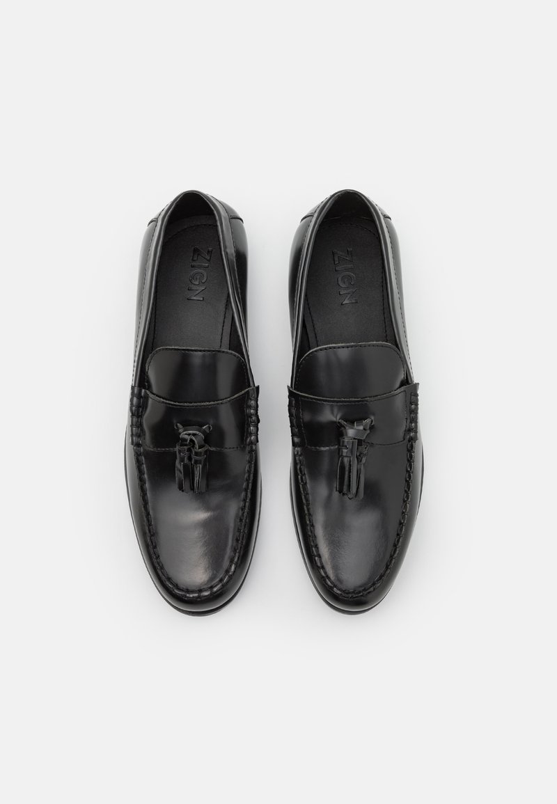 Mocasines de cuero negro con borlas decorativas, costura al estilo mocasín y un acabado liso y pulido. Diseño ergonómico para mayor comodidad.