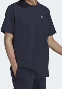 Marinblå bomullen t-shirt med rund halsringning, korta ärmar och en liten vit logotyp på bröstet. Tyget ser slätt och lätt ut.