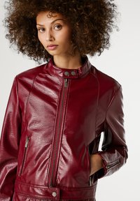 Bordeaux leren jas met een hoge kraag, rits aan de voorkant en zijzakken. Heeft metalen hardware en een gladde, glanzende textuur.
