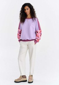 Heledat lilla pusa, millel on lillemustriga varrukad, sobitatud helevalgete pükstega ja beeźi värvi matkasaabastega. Pehme tekstuur, igapäevane disain.