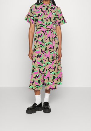 Kobieta w midi sukience z kołnierzykiem i krótkimi rękawami z abstrakcyjnym nadrukiem w kolorach różowym, zielonym, czarnym i beżowym, zestawiona z białymi skarpetkami i czarnymi loafersami.