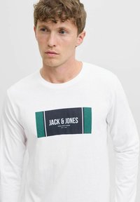 Ilgų rankovių balta marškinė suapvalinta iš medvilnės, kuriuose yra stačiakampis grafikas žalia ir tamsiai mėlyna spalvomis su "JACK & JONES" etikete. Paprasta tekstūra.