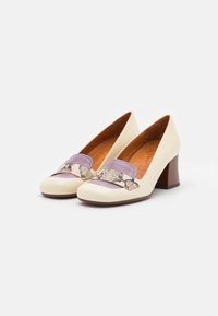 Chaussures pour femmes à talons bloc en crème avec des talons en bois marron, mettant en vedette des brides décoratives lilas et à motif serpent sur le devant.