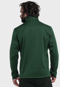 Green softshell jacket featuring a high collar, seamless shoulders, and textured material. Includes subtle branding and a fitted design.