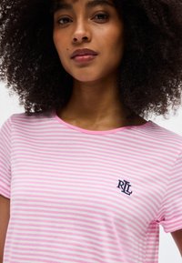 Νεαρή γυναίκα με σγουρά μαλλιά που φοράει ροζ και λευκή ριγέ μπλούζα με ένα μικρό ναυτικό λογότυπο "RL" στο στήθος.
