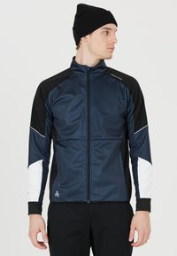 Marinblå och svart idrottsjacka med vita detaljer, dragkedja framtill, hög krage och långa ärmar. Tillverkad av mjukt, lätt tyg.