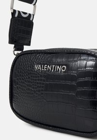 Svart krokodilpräglad läderväska med silverfärgad "VALENTINO"-logotyp, utrustad med ett mönstrat band och rektangulär form med slät yta.