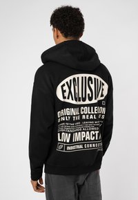 Black hoodie with a large white graphic print on the back featuring bold text and various phrases. Made from a soft material with a hood.