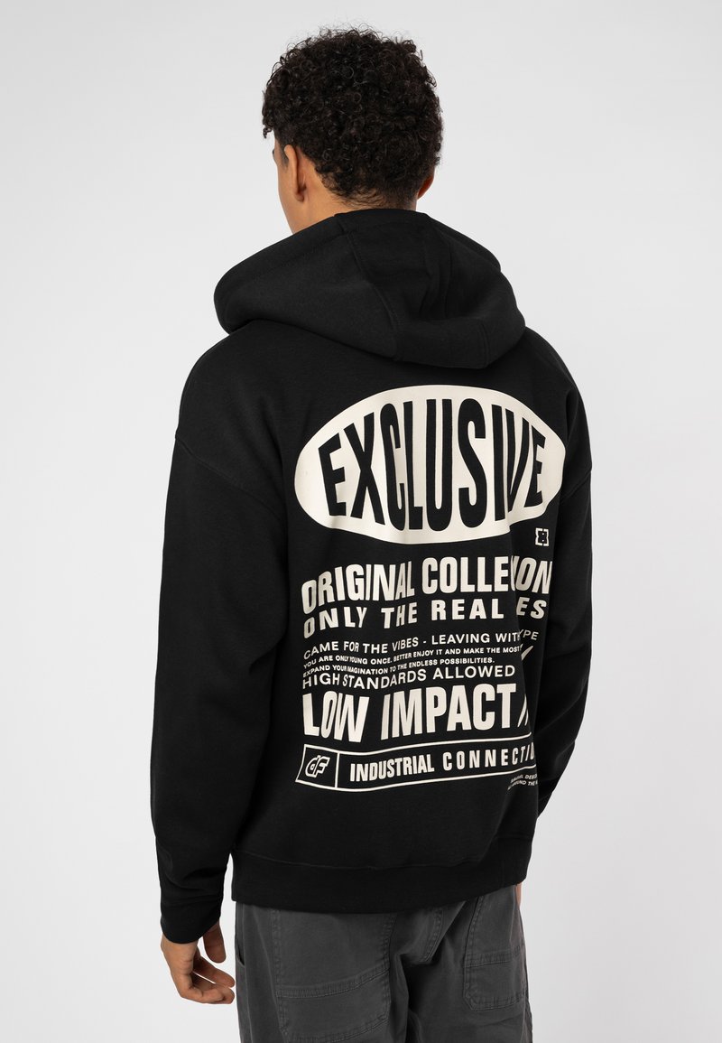 Black hoodie with a large white graphic print on the back featuring bold text and various phrases. Made from a soft material with a hood.