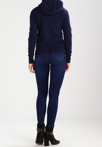 Mørkeblå hoodie med snor i hætten, båret med tætsiddende mørkeblå denim jeans og sorte ankelstøvler med spænde.