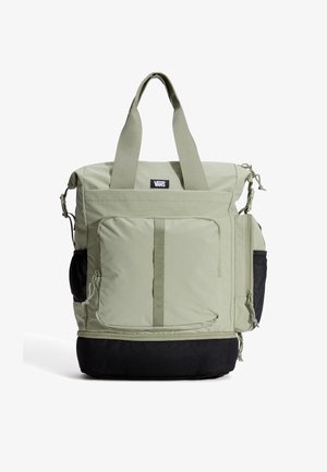 Zelená látková taška přes rameno s dvěma uchy a černým spodkem. Má několik kapes, zipů a na přední straně nášivku s logem.