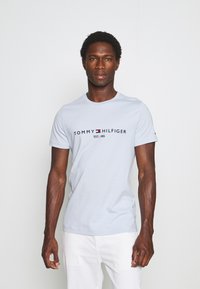 Šviesiai mėlyna trumpa rankovė T-marškiniai, pagaminti iš medvilnės, ant krūtinės su logotipu, kuriame parašyta "TOMMY HILFIGER" ir "EST. 1985" tamsiu spaudiniu.