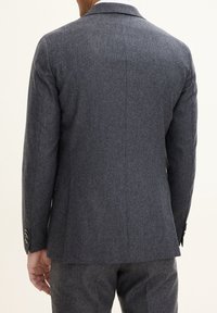 Blazer grigio in lana con design strutturato, rever a punta e due bottoni sui polsini. Caratterizzato da una fenditura singola sul retro per maggiore comfort.