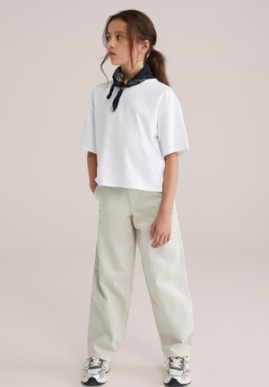 Weißes, kurz geschnittenes T-Shirt in übergroßer Passform, kombiniert mit hellgrünen, weit ausgestellten Hosen. Schwarzes Bandana um den Hals gebunden. Sportliche Sneakers mit Akzenten.