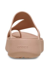 Sandales Crocs rose clair avec un bout arrondi, une semelle épaisse et des brides croisées en matériau doux et flexible. Logo "crocs" visible.