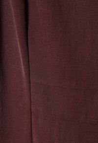 Tissu bordeaux foncé avec une finition texturée, affichant des lignes subtiles et une qualité de drapé douce. Aucun motif visible ni détail de quincaillerie.