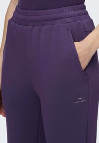 Lila Jogginghosen mit elastischem Bund, Seitentaschen und einem kleinen "Venice Beach"-Logo in Gold. Glatte Stoffstruktur.