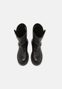 Botas de tornozelo em pele preta com biqueira arredondada, sola de borracha e detalhe de cinta ajustável. Textura suave e design simples e clean.