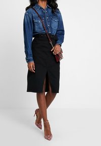 Chemise en denim avec patte de boutonnage et poches poitrine, associée à une jupe noire avec une fente frontale. Accentuée par des escarpins à motif serpent rose.