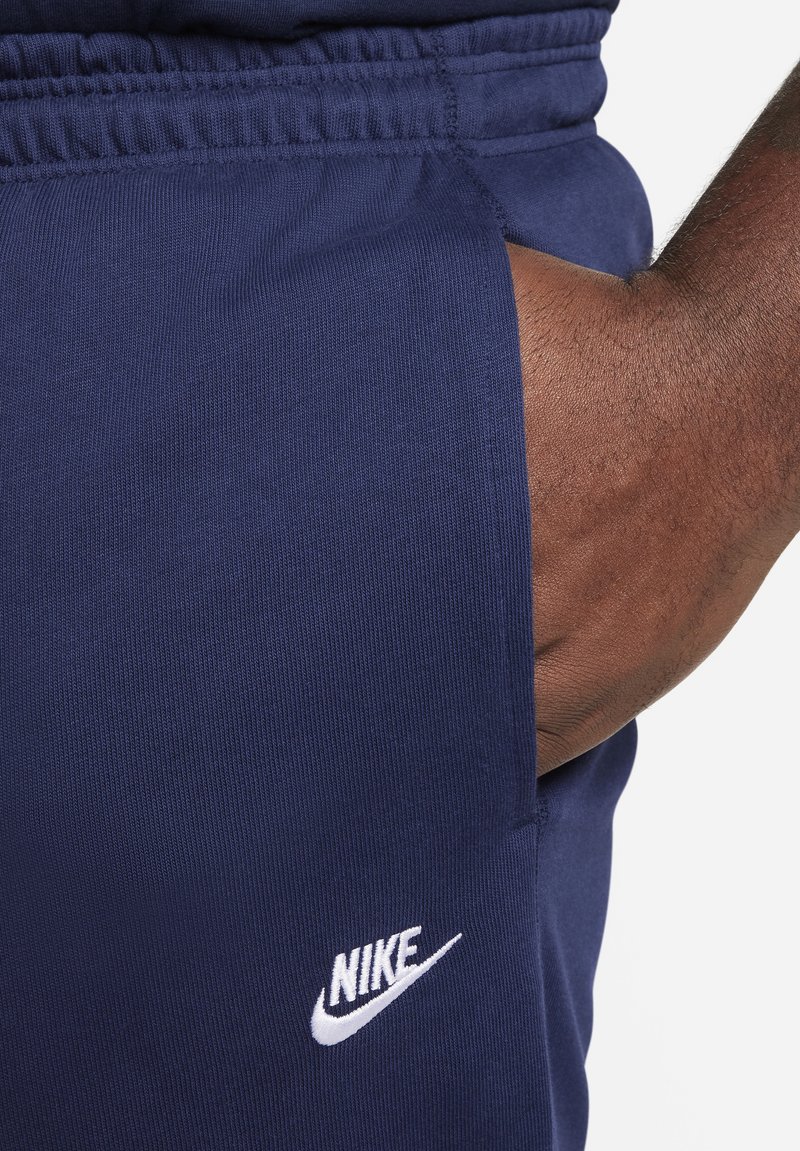 Pantalons de survêtement Nike bleu marine avec une texture côtelée, taille élastique et logo blanc près de la poche. Présente une coupe fuselée et une poche latérale.