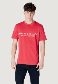 T-shirt rosso a maniche corte con la scritta bianca "Armani Exchange Milano/New York" sul petto; realizzato in tessuto morbido con una vestibilità classica.