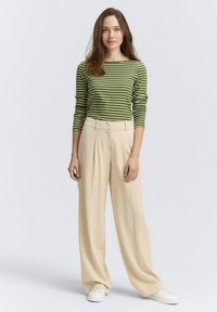 Gestreepte groene blouse met lange mouwen en ronde hals, gecombineerd met hoge, beige wijde broek en witte sneakers. Eenvoudige en relaxte pasvorm.