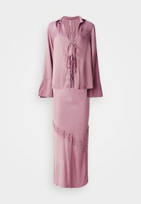 Abito due pezzi rosa composto da una blusa con laccetto frontale e dettagli in pizzo, abbinato a una gonna con un dettaglio in pizzo diagonale e uno spacco laterale.