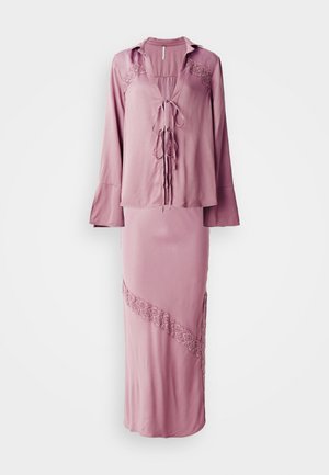 Abito due pezzi rosa composto da una blusa con laccetto frontale e dettagli in pizzo, abbinato a una gonna con un dettaglio in pizzo diagonale e uno spacco laterale.
