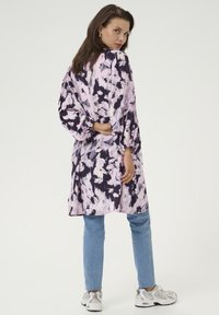 Blumenmuster-Kleid aus navyblauem und pinkfarbenem Stoff mit langen Ärmeln und lockerer Passform, kombiniert mit hellblauen Jeans und weißen Sneakers.