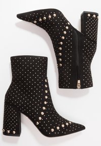 Mustat mokkanahkaiset nilkkasukat, joissa on terävä kärki ja palikkakorko, koristeltuna kultaisilla niiteillä ja sivuvetoketjulla.