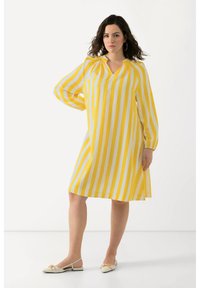 Abito a righe gialle e bianche con maniche lunghe, scollatura a V e tessuto morbido. Abbinato a delle scarpe slingback crema con dettaglio a fiocco.