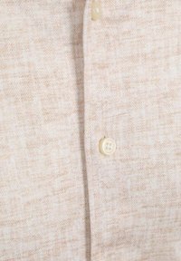 Beige textiel voor een overhemd met een subtiele geweven patroon, met een ronde, crèmekleurige knoop op de sluiting.