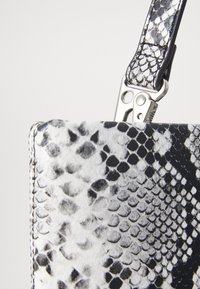 Black and white snake-print handbag with a textured surface and shiny silver hardware. The strap features a clip for attachment.