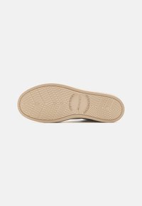 Sohle eines Sneakers, hellbraunes Gummi mit Zickzackprofil und kreisförmigem Logo. Glatte Oberfläche mit erhöhten Akzenten und Branding-Details.